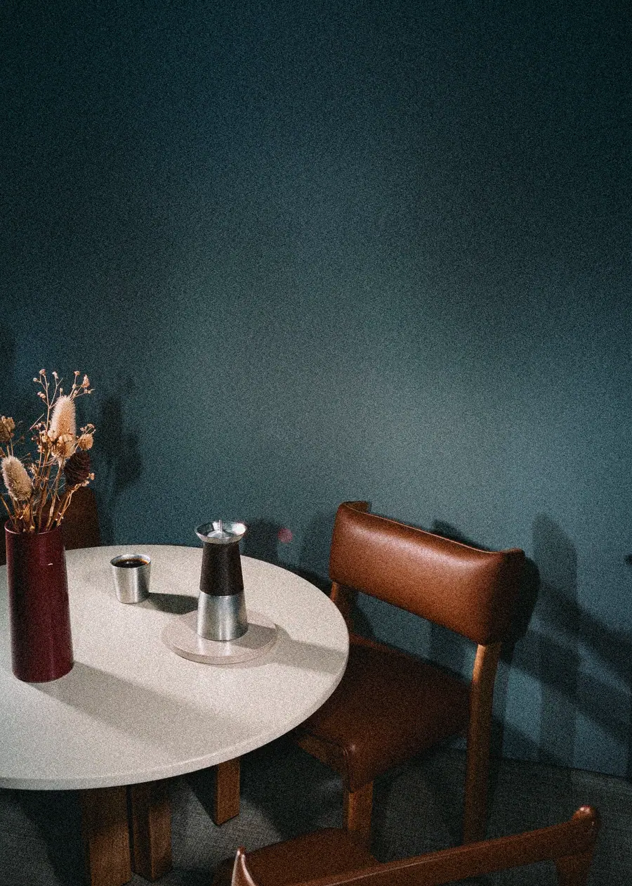 La cafetera Argo sobre una mesa redonda, junto a un jarrón con flores secas